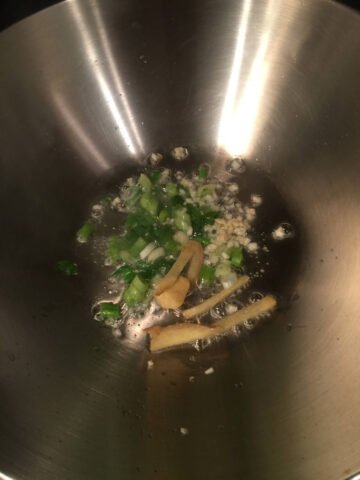 Chopped green onion, ginger and garlic are cooked in oil in a stainless steel wok
