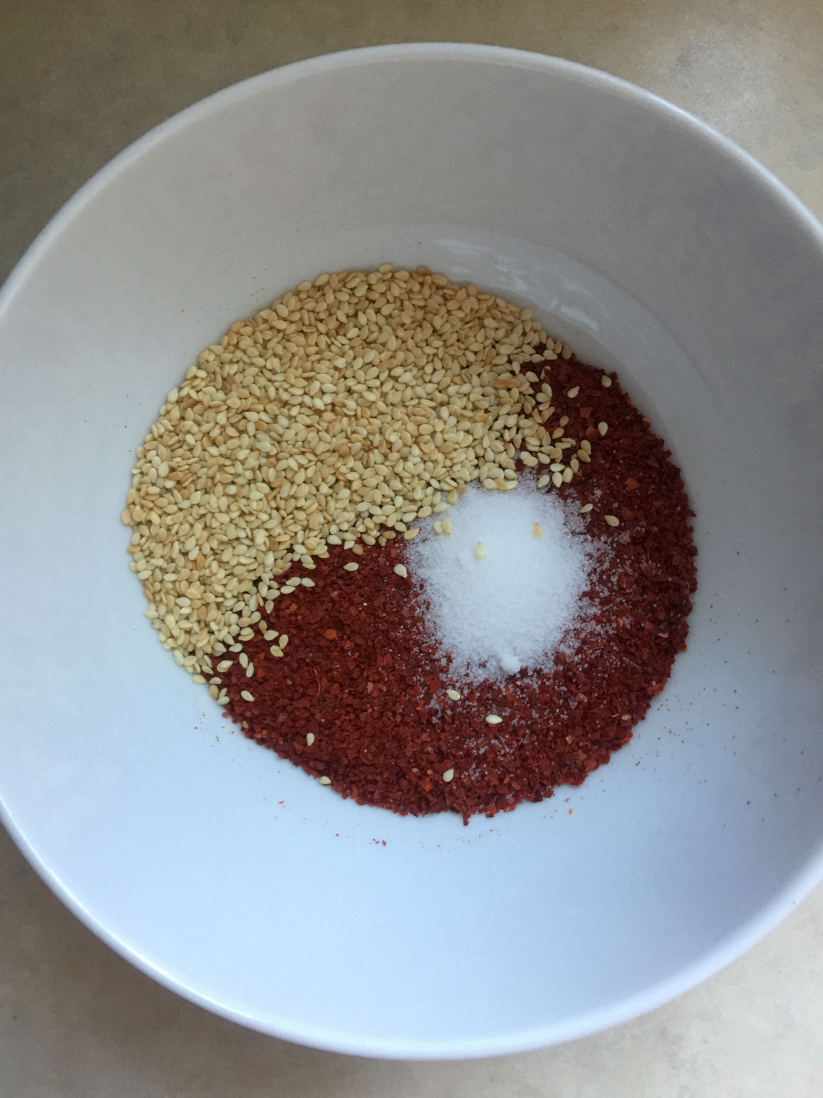 Overhead view of a white bowl with sesame seeds, salt and ground chili.