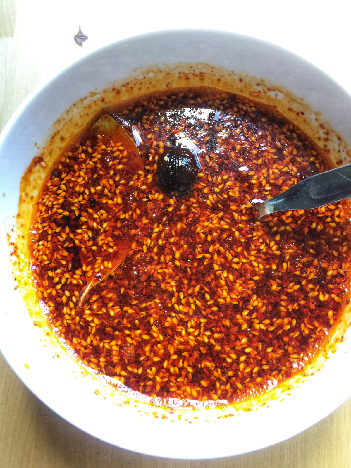 Overhead view of homemade chili oil in a white bowl placed on a wooden table.