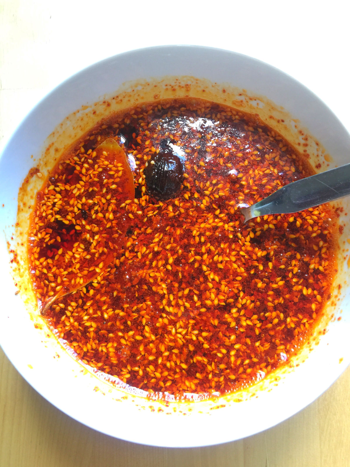 Overhead view of homemade chili oil in a white bowl with a spoon in the bowl.