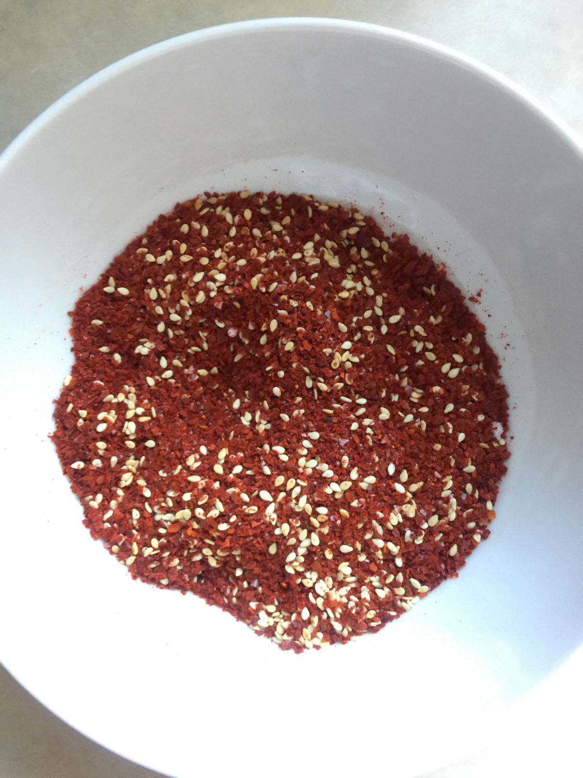 Overhead view of salt, sesame seeds and ground chili mixed together in a white bowl.