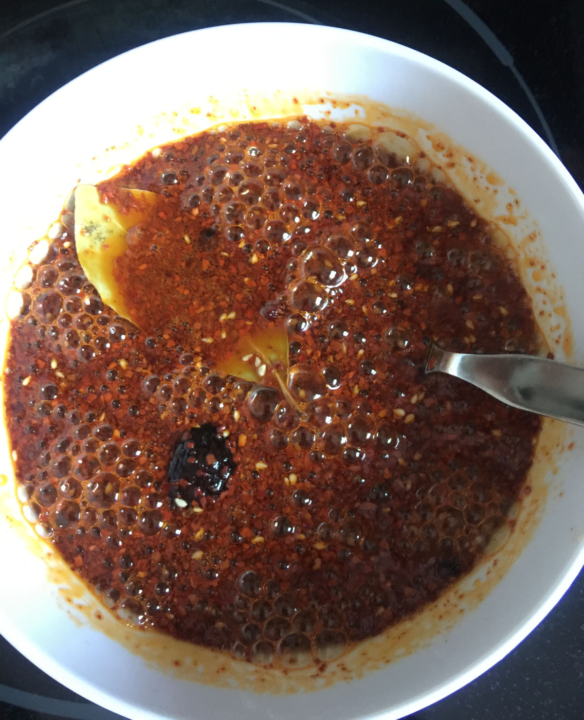 Overhead view of bubbles while pouring the hot oil into the seasonings in a white bowl.