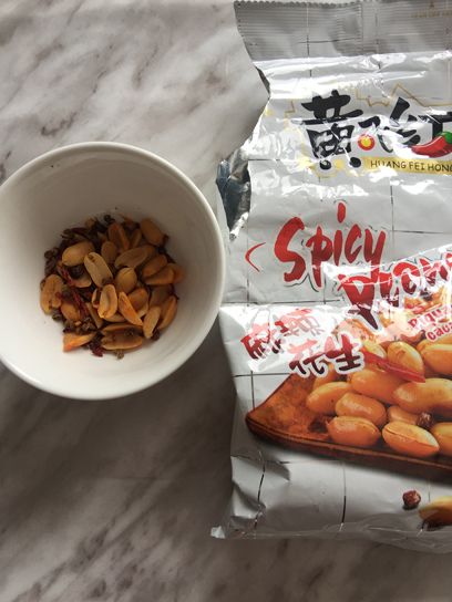 A package of store-bought roasted spicy peanuts and a small white bowl of the peanuts for demonstration.
