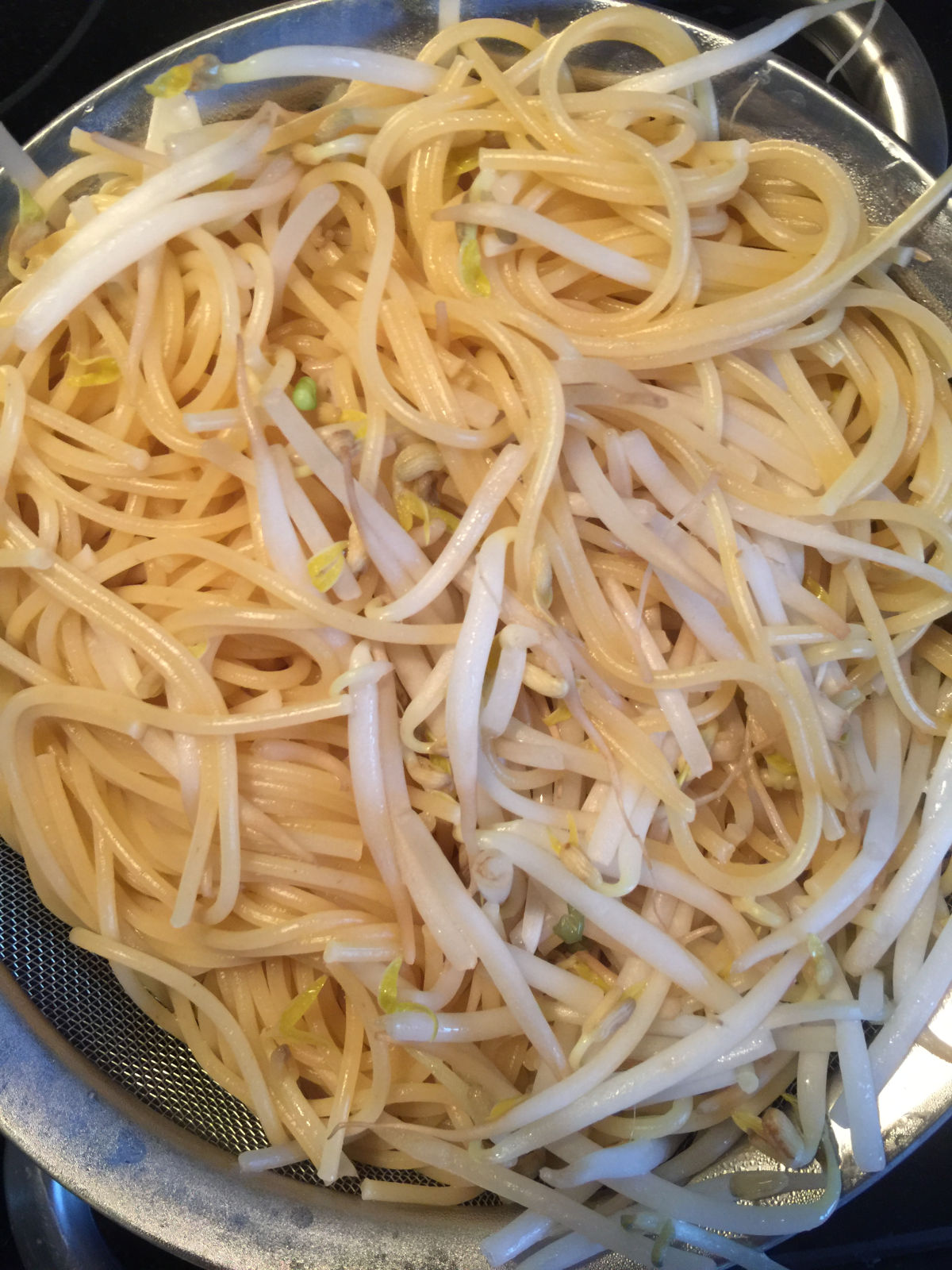 Overhead view of cooked spaghetti and soy bean sprouts draining in a strainer.