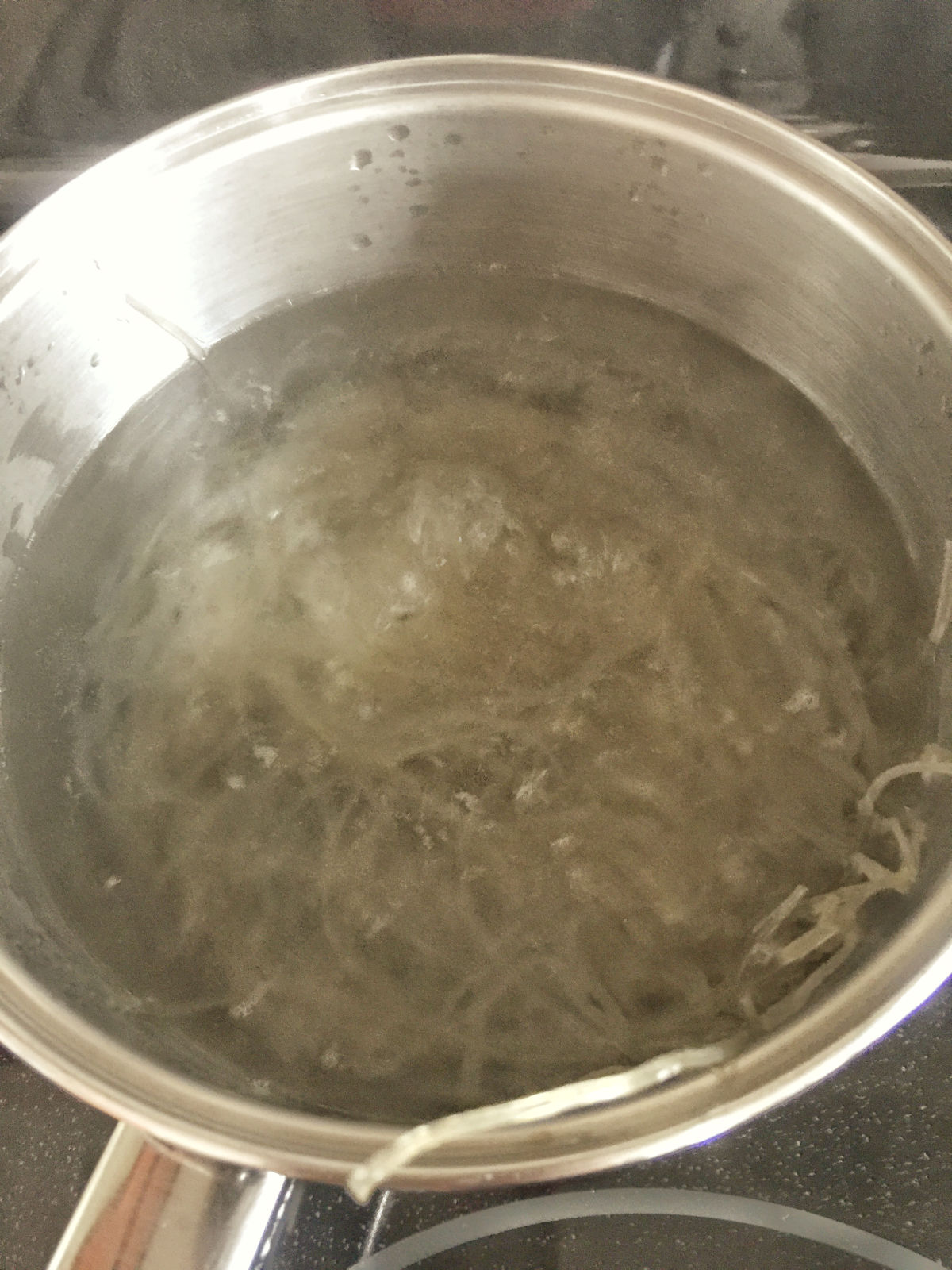 Sweet potato glass noodles in boiling water in a stainless steel pot on stove.