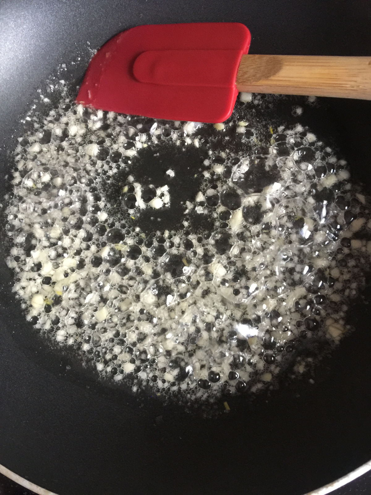 Close up view of minced garlic cooking in melt lard in a black non-sticky pan.