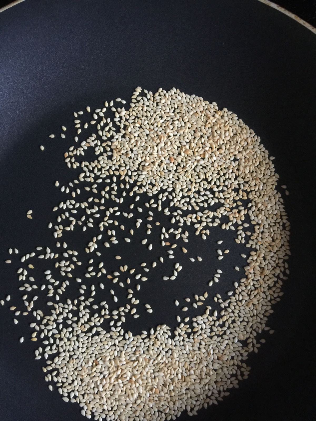 Overhead view of toasted sesame seeds in a black non-sticky pan.