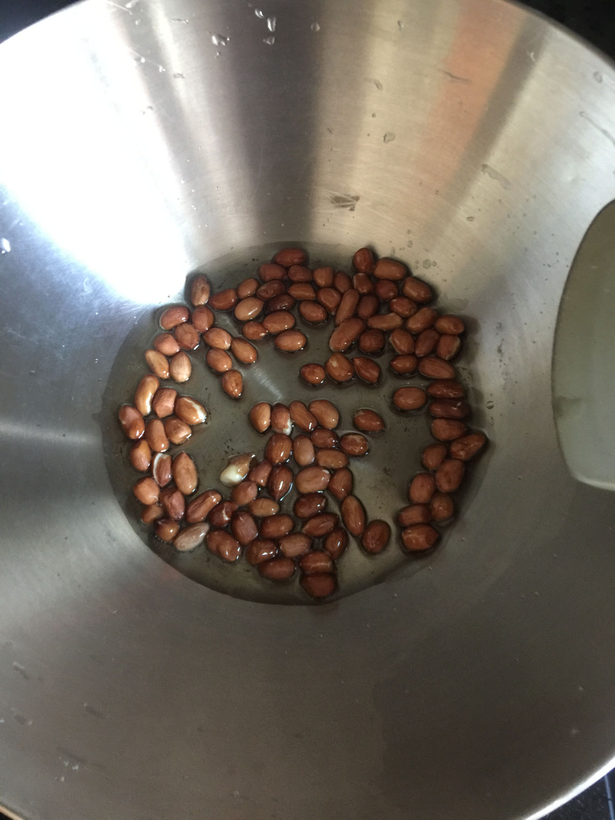 Overhead view of cooking peanuts in the oil in a wok.