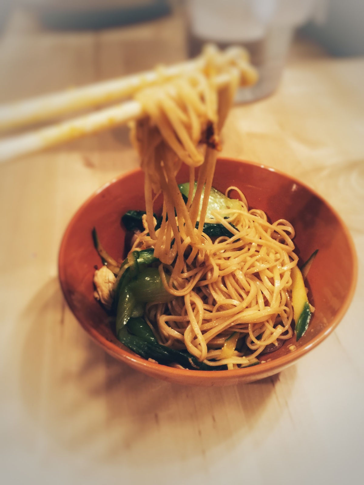 Side view of cold noodle with chicken shreds in an orange bowl, chopsticks picking up noodles.