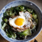Close up view of vegetable noodle soup in a bowl with a fried egg on top