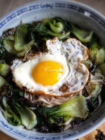Close up view of vegetable noodle soup in a bowl with a fried egg on top