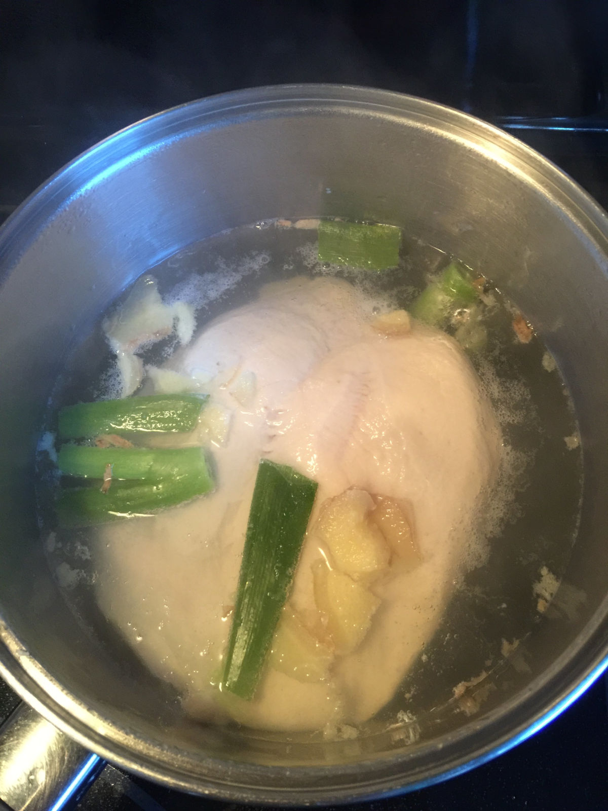 Chicken breast, green onion, slices of ginger in boiling water in pot.