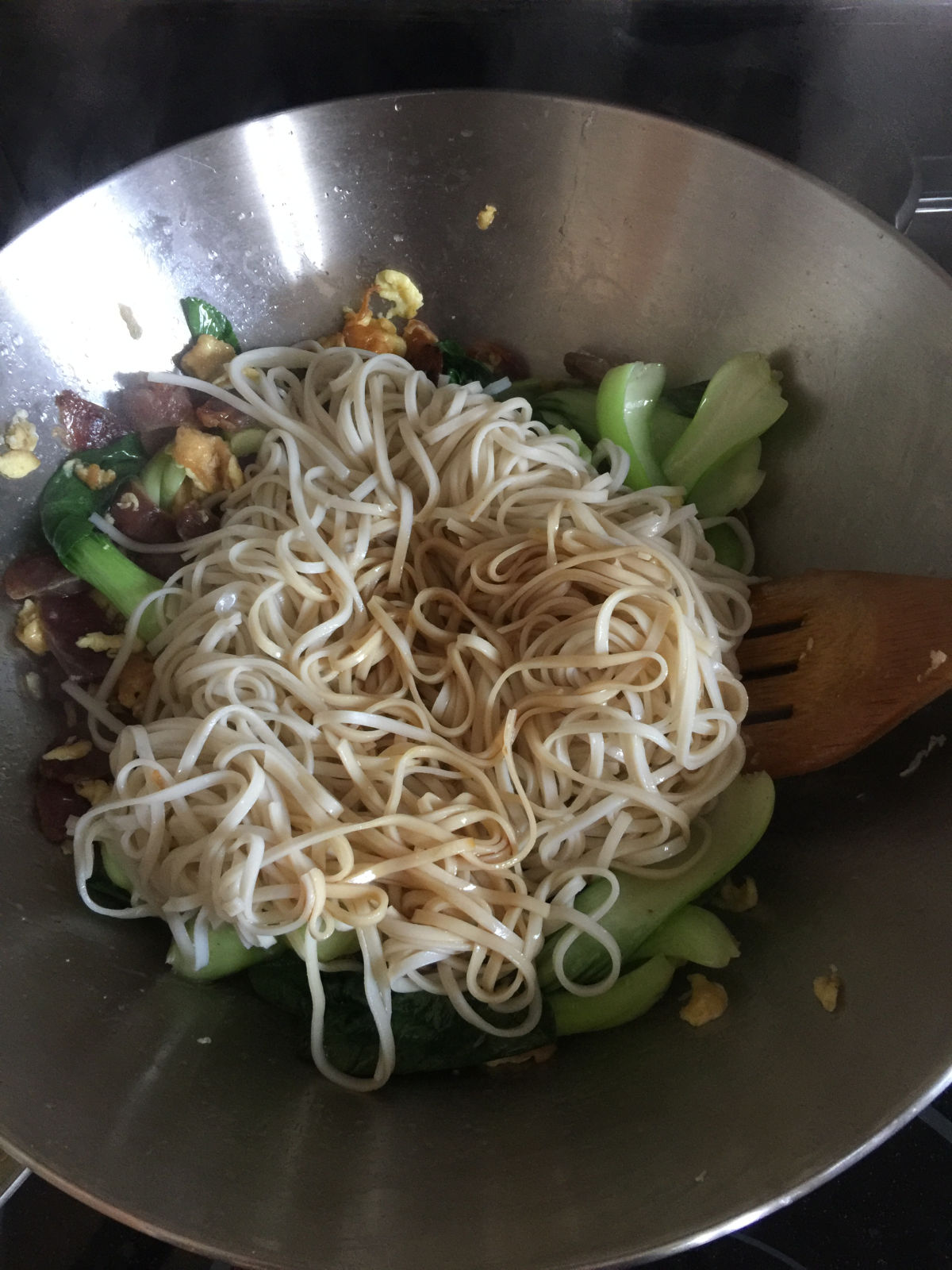 Noodles cooked with bok choy, eggs and sausages in wok.