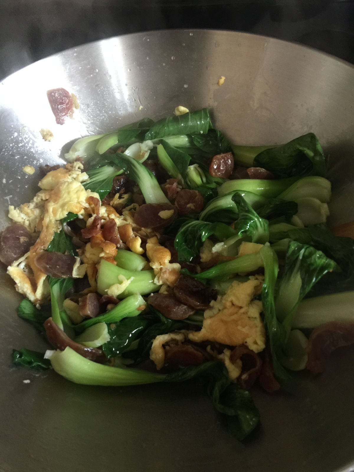 Bok choy cooked with eggs and sausages in wok.
