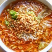 A close-up view of a white bowl of cooked Chongqing noodle soup with crushed peanuts on top.