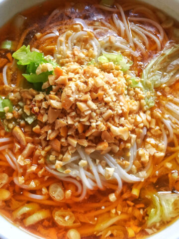 A close-up view of a white bowl of cooked Chongqing noodle soup with crushed peanuts on top.