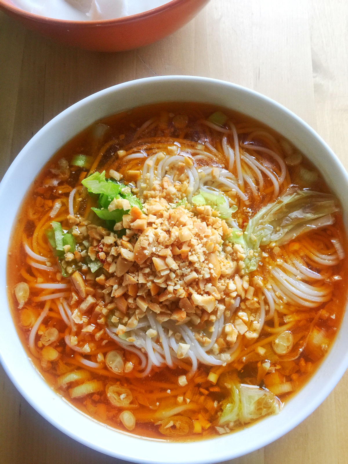 Overhead view of a white bowl of Chongqing noodle soup topped with crushed peanuts next to the lard placed in an orange bowl.
