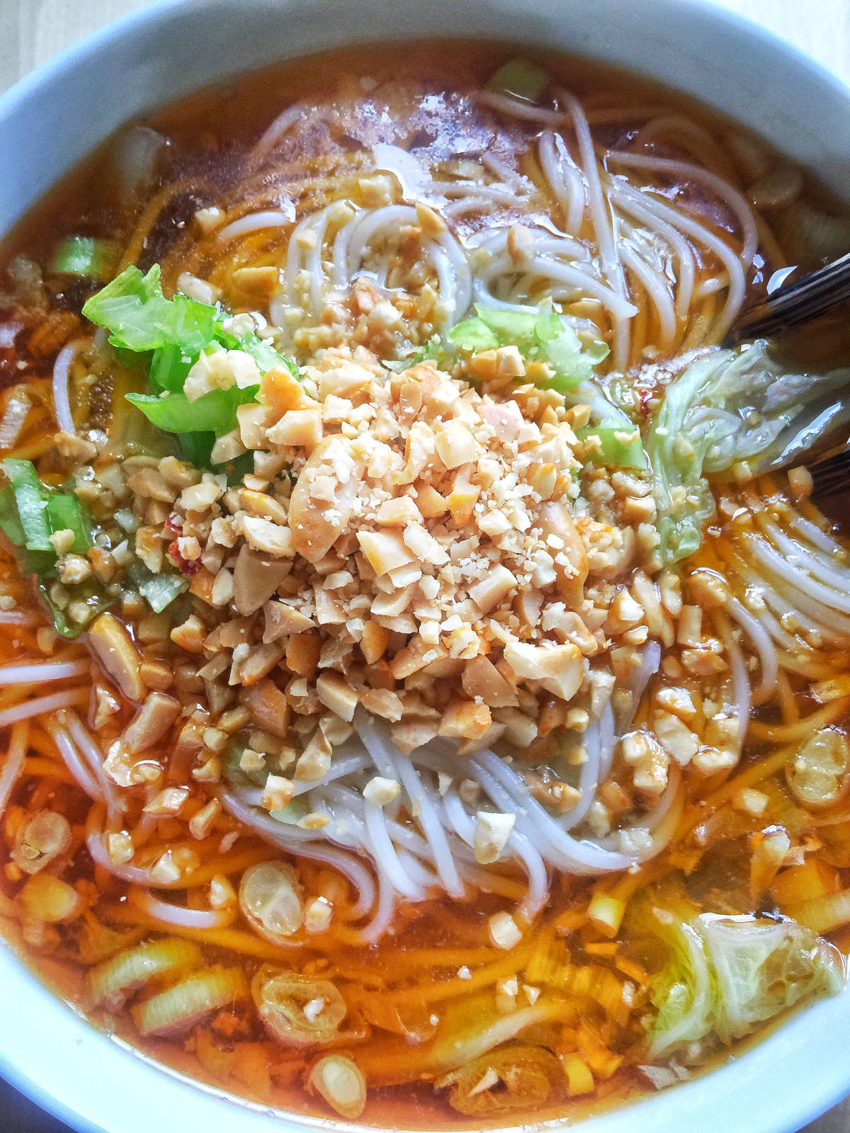 A close-up view of a bowl of Chongqing spicy noodles topped with chopped peanuts with chopsticks on the side.