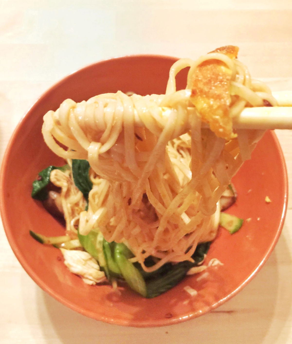 Close-up view of finished cold noodles with shredded chicken in orange bowl with chopsticks.