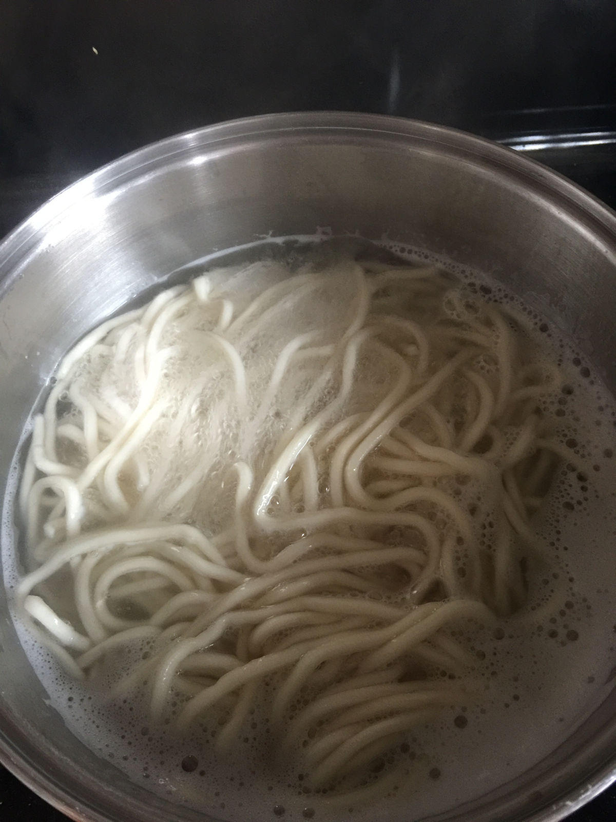 Overhead view of Shanghai thick noodles cooking in boiling water in a pot.