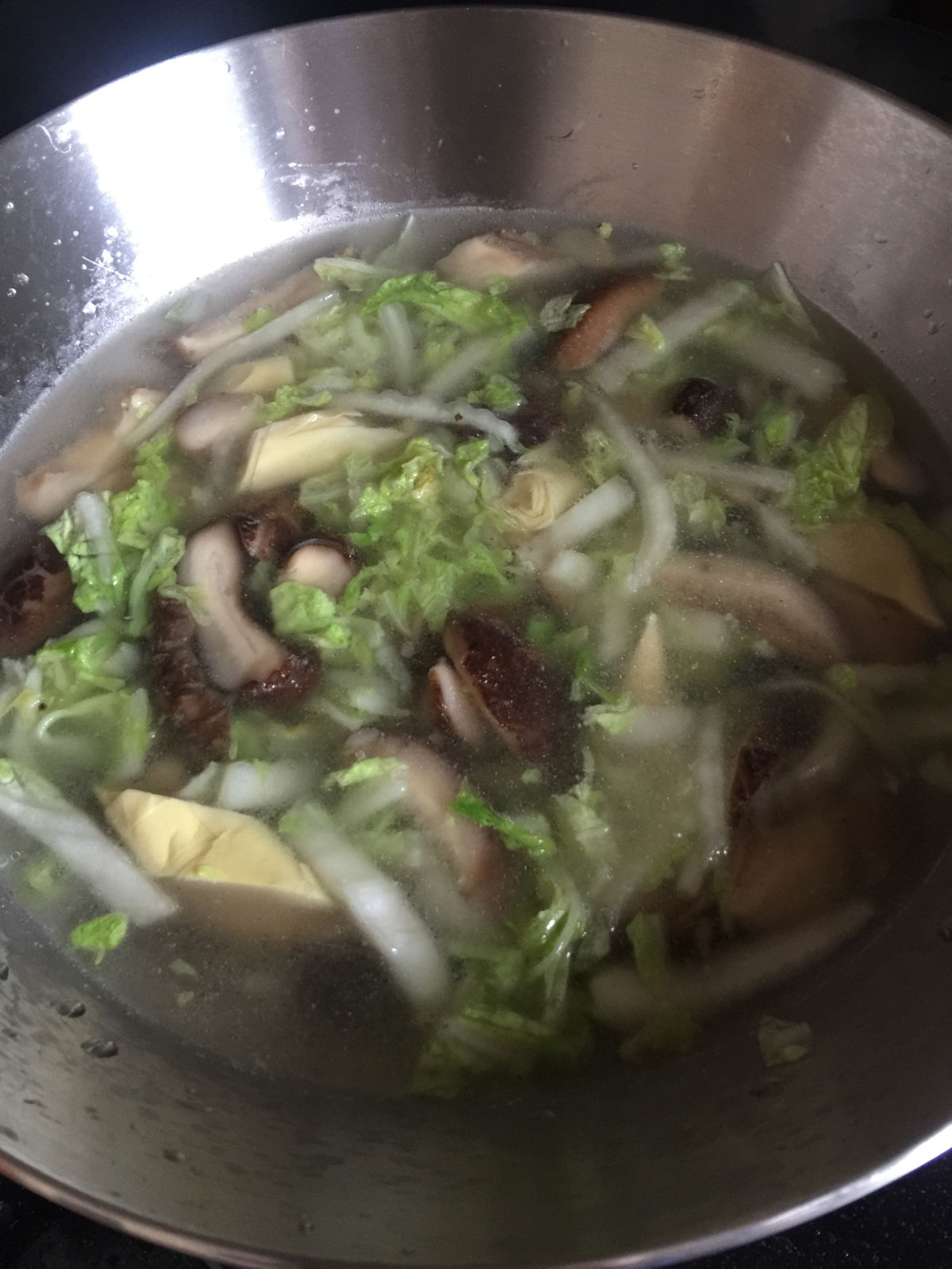 A close up view of vegetables soup cooking in a stainless steel wok.