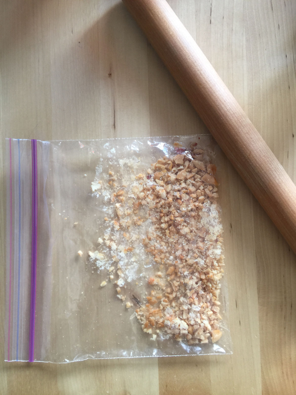 Overhead view of crushed peanuts in a Ziploc bag with a rolling pin on the side. 