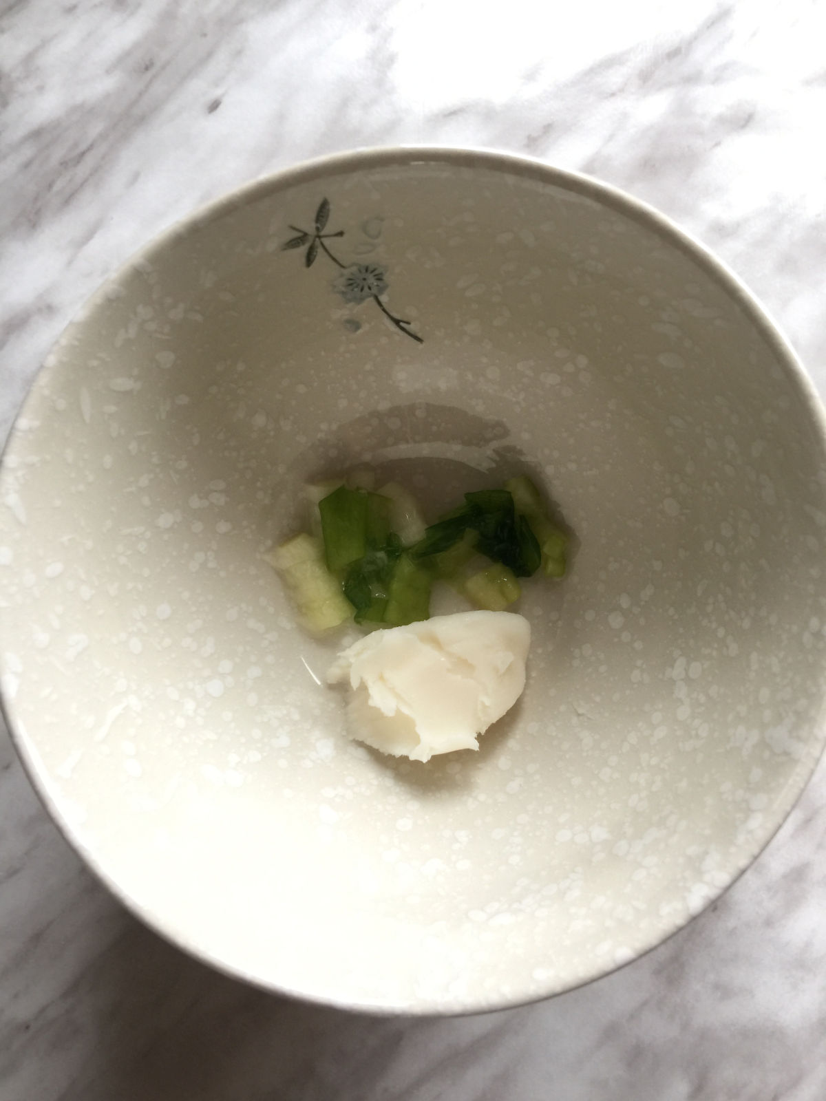 Overhead view of a bowl with finely chopped green onion and a small chunk of lard.