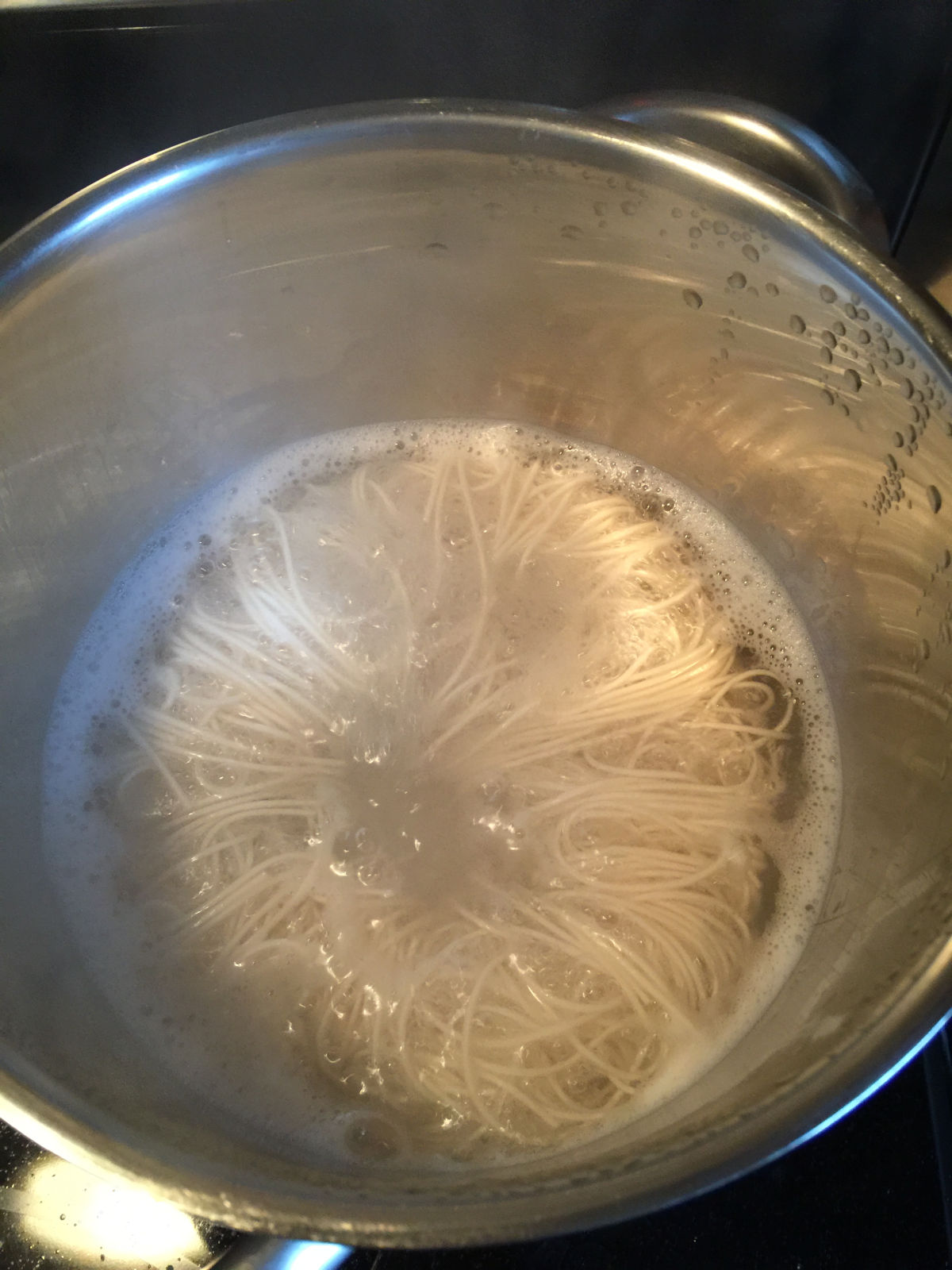Overhead view of boiling noodles in a stainless steel pot.