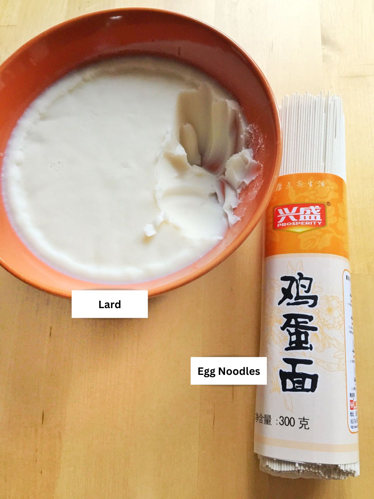 Close up view of a bowl of lard and a bundle of thin egg noodles - labeled ingredients.