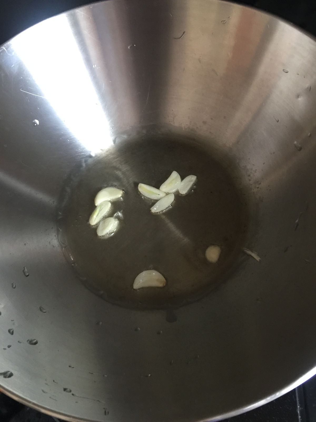 Overhead view of garlic slices saute in stainless steel wok.