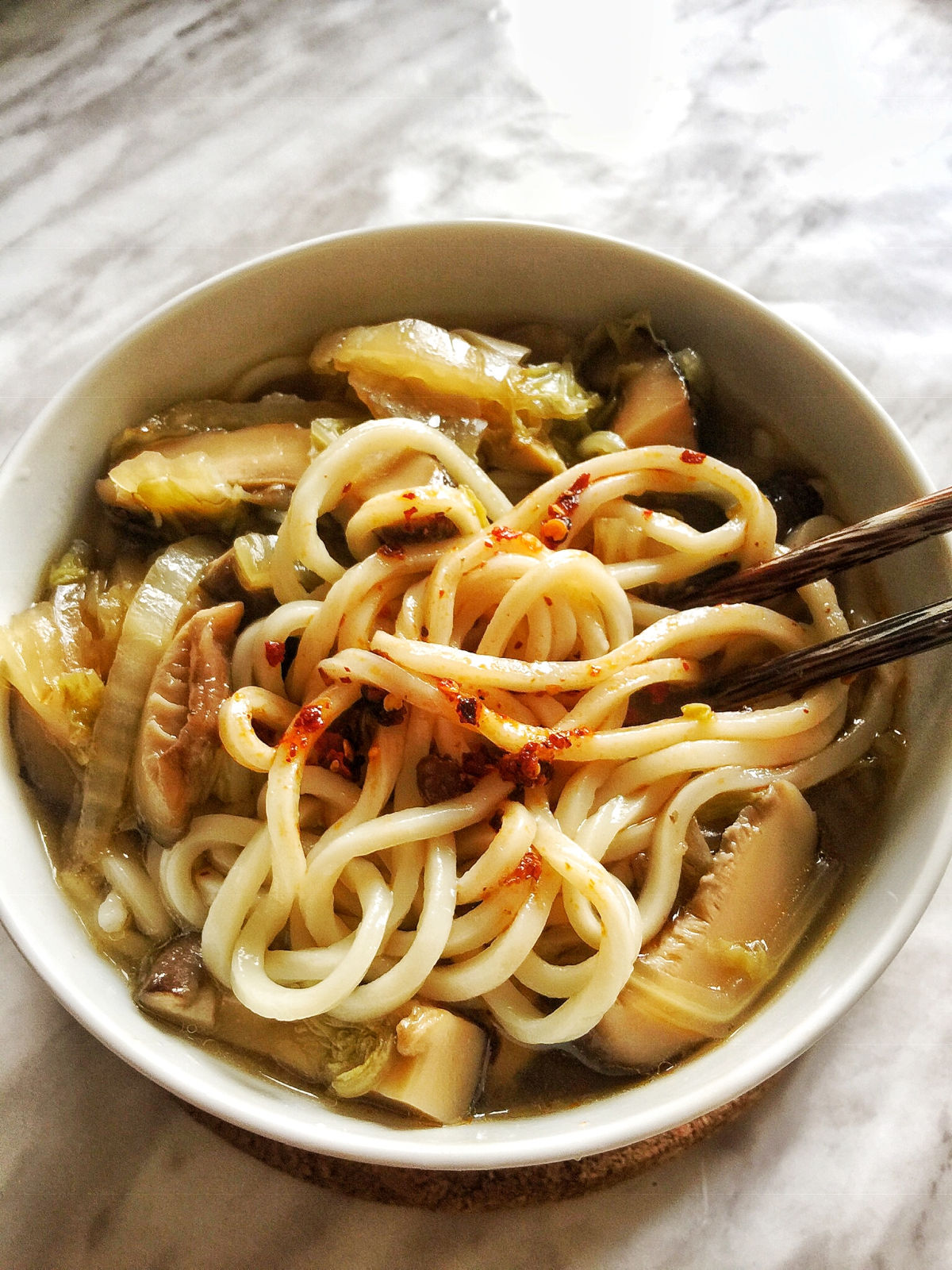 Overhead view of a bowl of cooked vegetable noodle soup with Lao Gan Ma chili crisp on top.